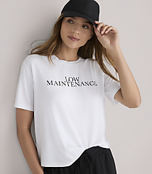 A woman in a white t-shirt with "LOW MAINTENANCE" printed on it and black shorts stands against a plain white background. carousel Product Image 2