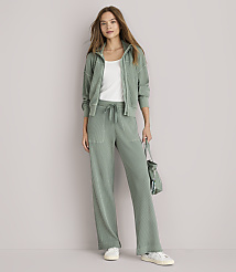 A woman in a sage green loungewear set stands against a plain white background, holding a matching bag. carousel Product Image 1