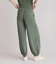 A person wearing loose-fitting green sweatpants and light-colored sneakers stands against a plain white background. carousel Product Image 3