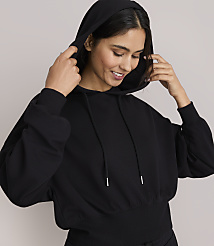 A smiling woman in a black hoodie adjusts the hood against a plain gray background. carousel Product Image 2