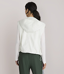 A woman in a white hooded vest and green pants stands against a plain white background. carousel Product Image 3
