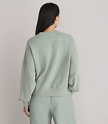 A woman in a light green sweatshirt and pants stands with her back to the camera against a plain white background. carousel Product Image 3