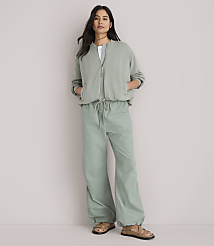 A woman stands in the foreground wearing a sage green bomber jacket and matching wide-leg pants, against a plain white background. carousel Product Image 2