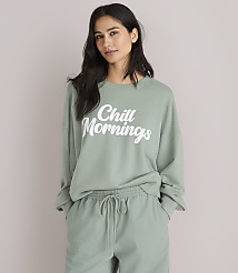 A woman in a green sweatshirt and pants sits against a plain white background. carousel Product Image 1