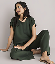 A woman in a dark green loungewear set sits on a white floor, looking to the side with a plain white background. carousel Product Image 2
