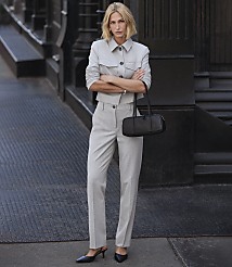 A woman in a light gray suit stands with her arms crossed in front of a dark brick building. carousel Product Image 6