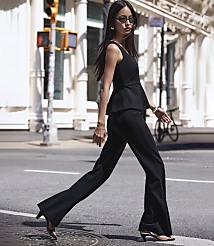 A woman in a black peplum top and flared pants walks across a street with a traffic light and buildings in the background. carousel Product Image 6