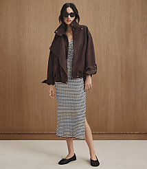 A woman in a brown jacket and striped dress stands against a wood-paneled background. carousel Product Image 4