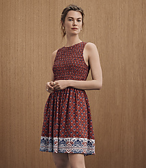 A woman in a patterned red dress stands against a textured brown background. carousel Product Image 4