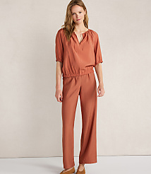 A woman in a rust-colored jumpsuit stands against a plain, light-colored wall. carousel Product Image 2