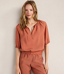 A woman in a rust-colored top and pants stands against a plain, light-colored wall. carousel Product Image 1