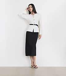 A woman in a white jacket and black skirt stands against a white wall with a light gray floor in the foreground. carousel Product Image 1