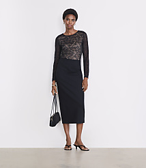 A woman in a black lace top and pencil skirt stands against a plain white background, holding a small black purse. carousel Product Image 1