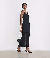 A woman in a black dress and sandals stands against a plain white background, holding a small black purse. carousel Product Image 1