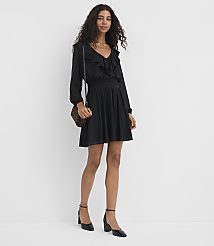 A woman in a black ruffled dress and heels stands against a plain white background, carrying a patterned crossbody bag. carousel Product Image 1