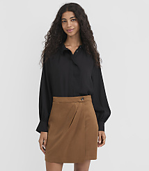 A woman with long, dark, curly hair stands in the foreground wearing a black blouse and a brown skirt, against a plain white background. carousel Product Image 2