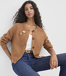 A woman in a brown cardigan and blue jeans sits against a plain white background. carousel Product Image 1