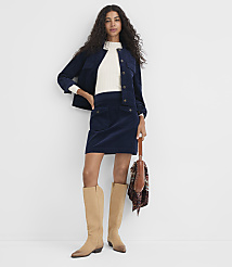 A woman in a navy corduroy skirt and jacket stands against a plain white background, holding a patterned scarf and wearing tan boots. carousel Product Image 1
