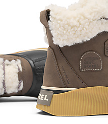 A close-up of a brown Sorel boot with a fluffy white lining is in the foreground, while another boot is blurred in the background. carousel Product Image 6