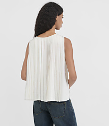 A woman in a white pleated top and blue jeans stands against a plain white background. carousel Product Image 3