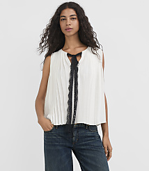 A woman in a white pleated top with black lace trim and dark jeans stands against a plain white background. carousel Product Image 1