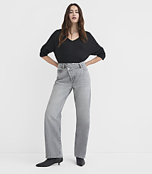 A woman in a black v-neck shirt and grey criss-cross jeans stands against a plain white background. carousel Product Image 1