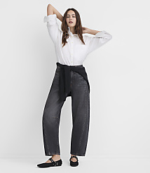 A woman in a white blouse and dark jeans stands with her arms behind her head against a plain white background. carousel Product Image 1
