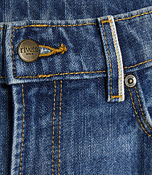 A close-up of blue denim jeans features a brass button with "rivete DENIM" on the left and a small metal rivet on the right, with yellow stitching throughout. carousel Product Image 4