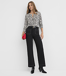 A woman in a black and white spotted blouse and black wide-leg pants stands against a plain white background, holding a red clutch. carousel Product Image 1