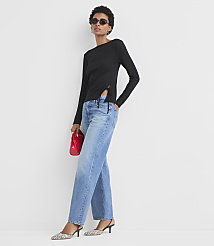 A woman in a black top and blue jeans stands against a plain white background, holding a red clutch. carousel Product Image 2