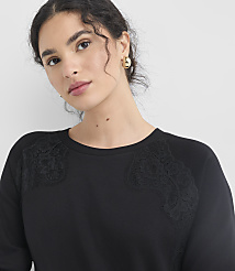 A woman with dark curly hair and gold earrings wears a black sweatshirt with lace detailing on the shoulders, set against a plain white background. carousel Product Image 4