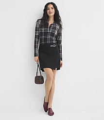 A woman in a plaid shirt and black skirt stands against a plain white wall, holding a small leopard-print purse. carousel Product Image 2