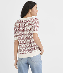 A woman in a cream and red wavy-patterned sweater and light blue jeans stands against a plain white background. carousel Product Image 3