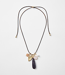 A delicate brown cord necklace with various charms, including a heart and a teardrop-shaped stone, hangs against a plain white background. carousel Product Image 1
