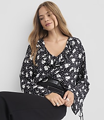 A woman in a black and white floral blouse with ruffled neckline and bell sleeves poses against a plain gray background. carousel Product Image 2