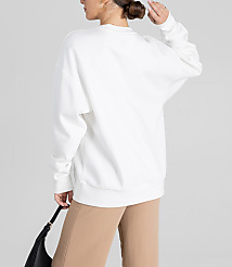 A woman in a white sweatshirt and tan pants holds a black purse against a plain gray background. carousel Product Image 2