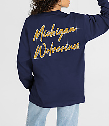 A person in a navy long-sleeved shirt with "Michigan Wolverines" in gold glitter on the back stands against a plain white background. carousel Product Image 2
