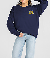 A woman in a navy sweatshirt with a gold "M" logo and light-wash jeans stands against a plain white background. carousel Product Image 1