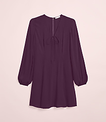A plum-colored dress with a tie-neck detail and balloon sleeves hangs against a soft pink background. carousel Product Image 4