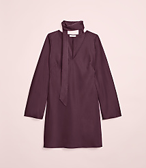 A plum-colored dress with a tie neck is laid flat against a soft pink background. carousel Product Image 2