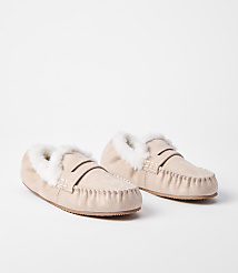 A pair of light beige moccasin slippers with fluffy white lining rests on a plain white background. carousel Product Image 1