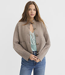 A young woman in a beige cardigan and blue jeans stands against a plain white background. carousel Product Image 2