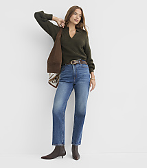 A woman in a green sweater and blue jeans stands against a plain white background, holding a brown bag over her shoulder. carousel Product Image 3