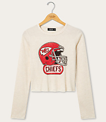 A cream-colored long-sleeved shirt with a distressed Kansas City Chiefs helmet graphic is displayed on a wooden hanger against a plain white background. carousel Product Image 1