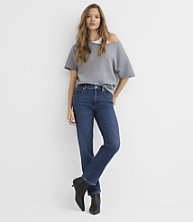 A woman in a gray off-the-shoulder top and dark wash jeans stands against a plain white background. carousel Product Image 1