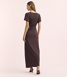 A woman in a dark purple, ruched maxi dress stands against a soft pink background. carousel Product Image 4