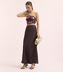 A woman in a strapless floral top and a long skirt poses with a gold clutch against a soft pink background. carousel Product Image 1