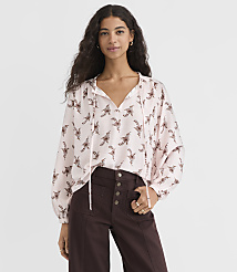 A woman in a light pink, patterned blouse and dark brown pants stands against a plain white background. carousel Product Image 1