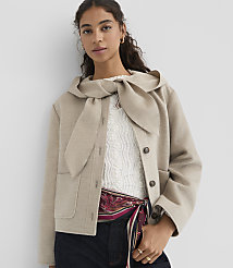 A woman in a beige jacket with a large bow collar stands against a plain white background. carousel Product Image 2