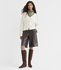 A woman in a cream cable-knit cardigan, brown leather culottes, and brown boots stands against a plain white background. carousel Product Image 1